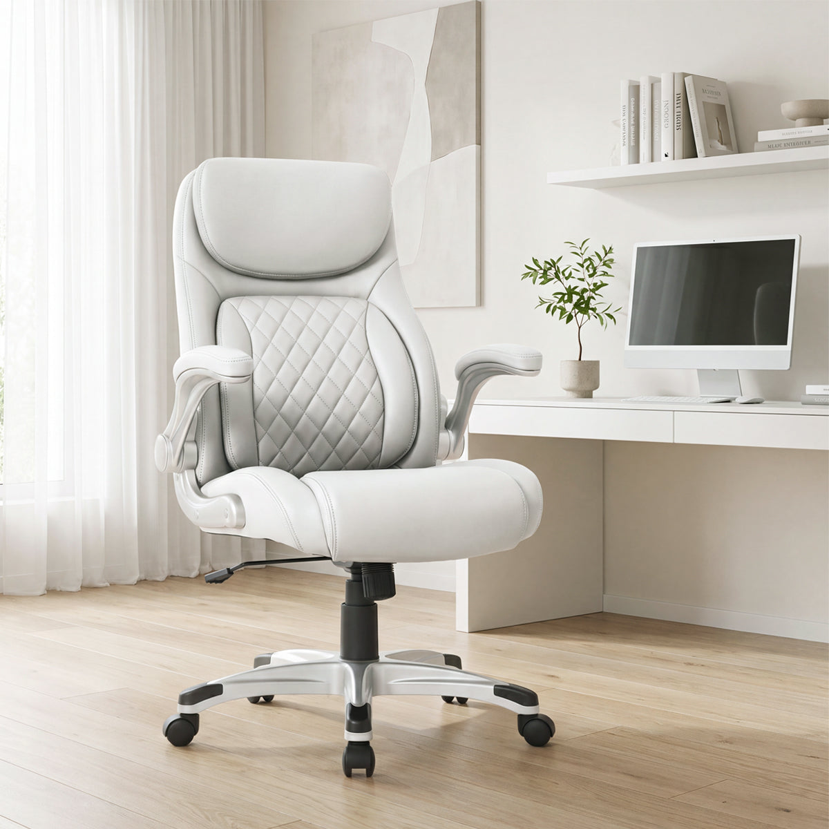 NHO-0004WH, Flat White ergonomic executive office chair in a bright, modern American home office during a sunny daylight saving time afternoon. The premium off-white leather chair features a diamond-quilted backrest, padded flip-up armrests, and a sleek silver base with casters, resting on light hardwood floors. In the background, warm natural sunlight streams through sheer curtains, illuminating a minimalist white desk with a computer, potted plant, floating shelves with books, and abstract wall art.