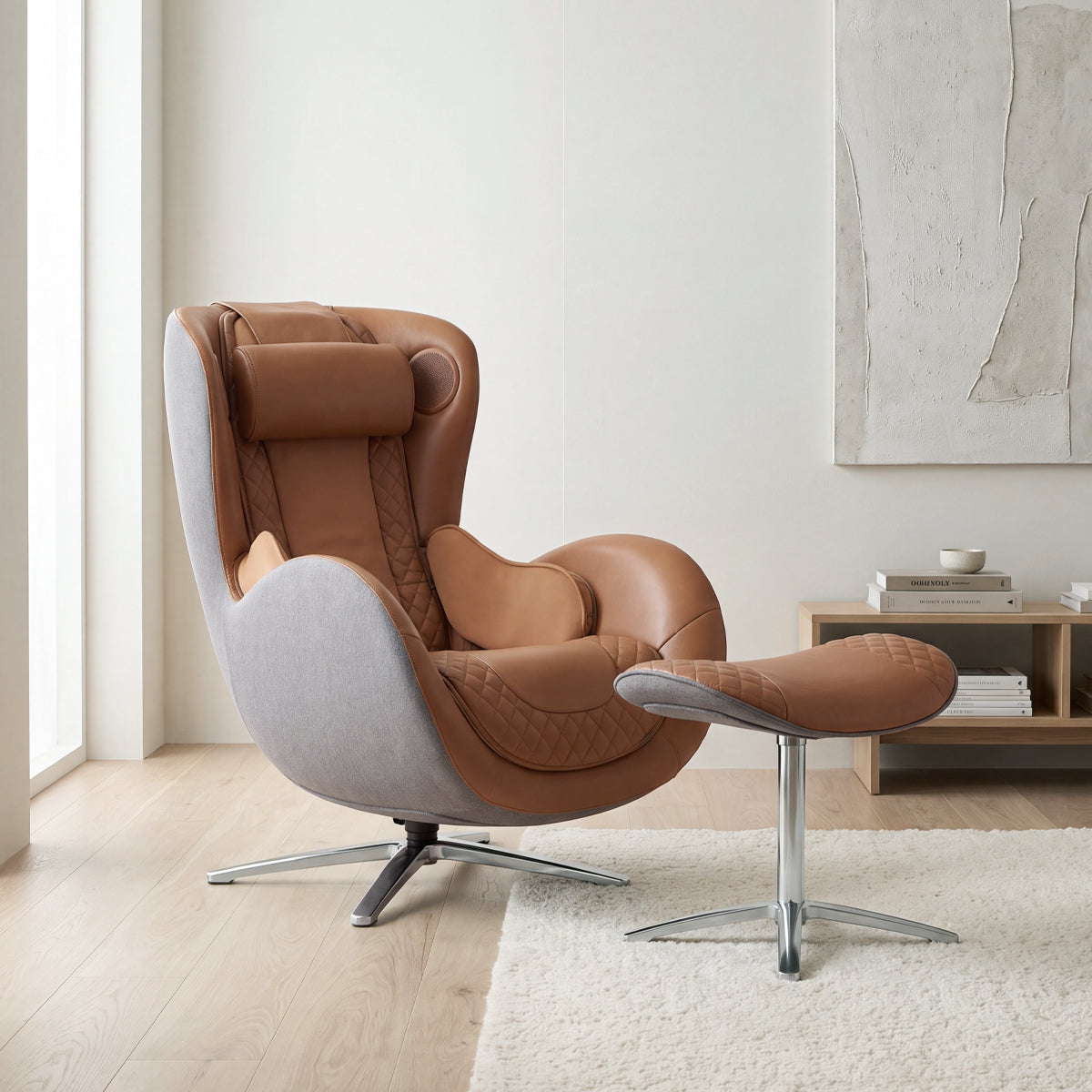 N-0003CR-V2, Caramel ergonomic massage recliner with its matching ottoman, set within a serene, sunlit minimalist living room with wood flooring, an off-white rug, a large window, a low-profile wood storage console with books, and an abstract textured wall painting.