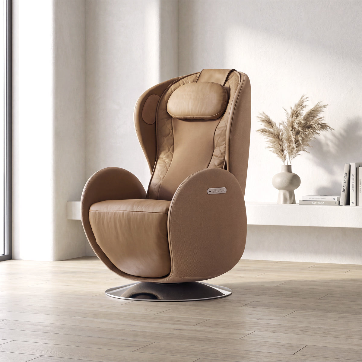 NR-SN100L-CM, Dark Caramel ergonomic massage armchair in a bright, modern American living room during a sunny daylight saving time afternoon. The elegant tan-brown leather and fabric lounger rests on light hardwood floors, featuring integrated side controls and a sleek circular metallic pedestal base. In the background, warm natural sunlight creates soft shadows on the white walls, illuminating a minimalist floating shelf adorned with books and a ceramic vase filled with fluffy pampas grass.