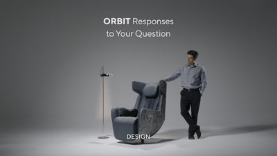 Video still of a man standing beside a modern dark gray ORBIT massage chair, with the text "ORBIT Responses to Your Question" and "DESIGN" displayed against a neutral gray background.